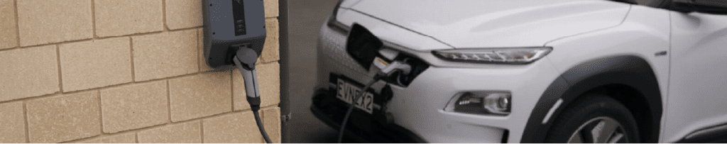 EV charger, connected to a brick wall charging a white car.